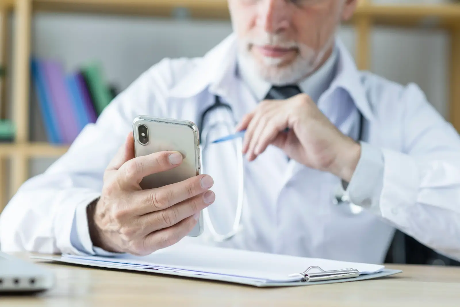 Médico de jaleco branco usando um smartphone no consultório